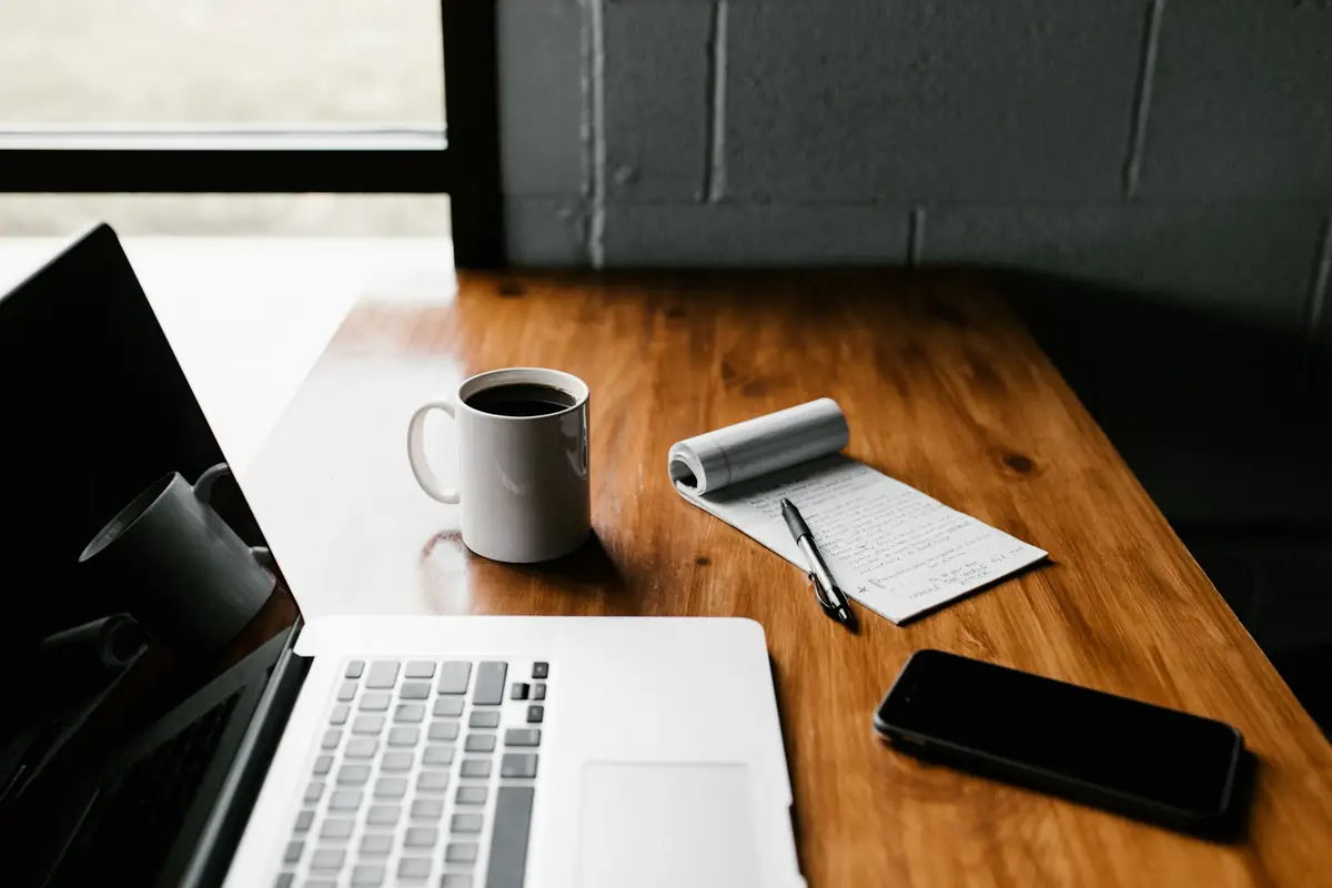 Laptop, coffee mug, notepad and smartphone on a wooden desk