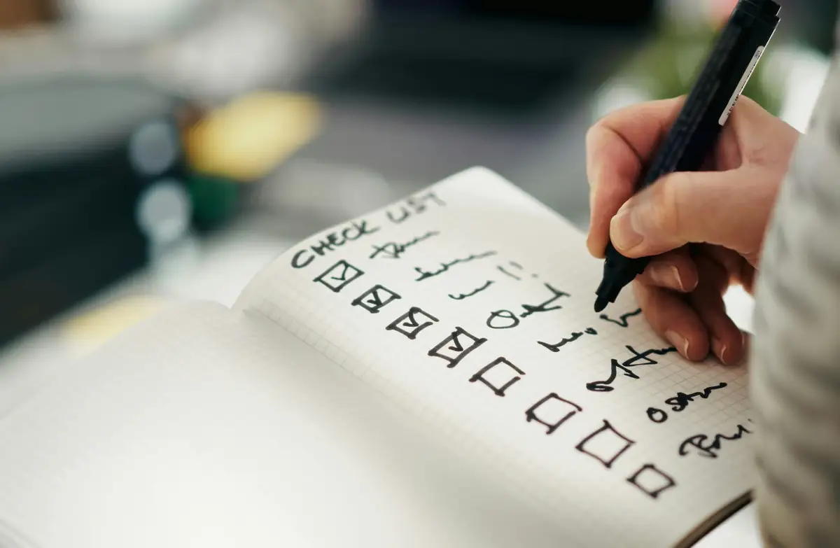 A hand writing a checklist with boxes in a notebook